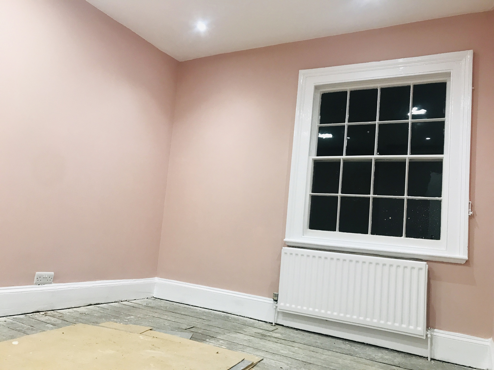 Blush pink room with a white sash window and radiator